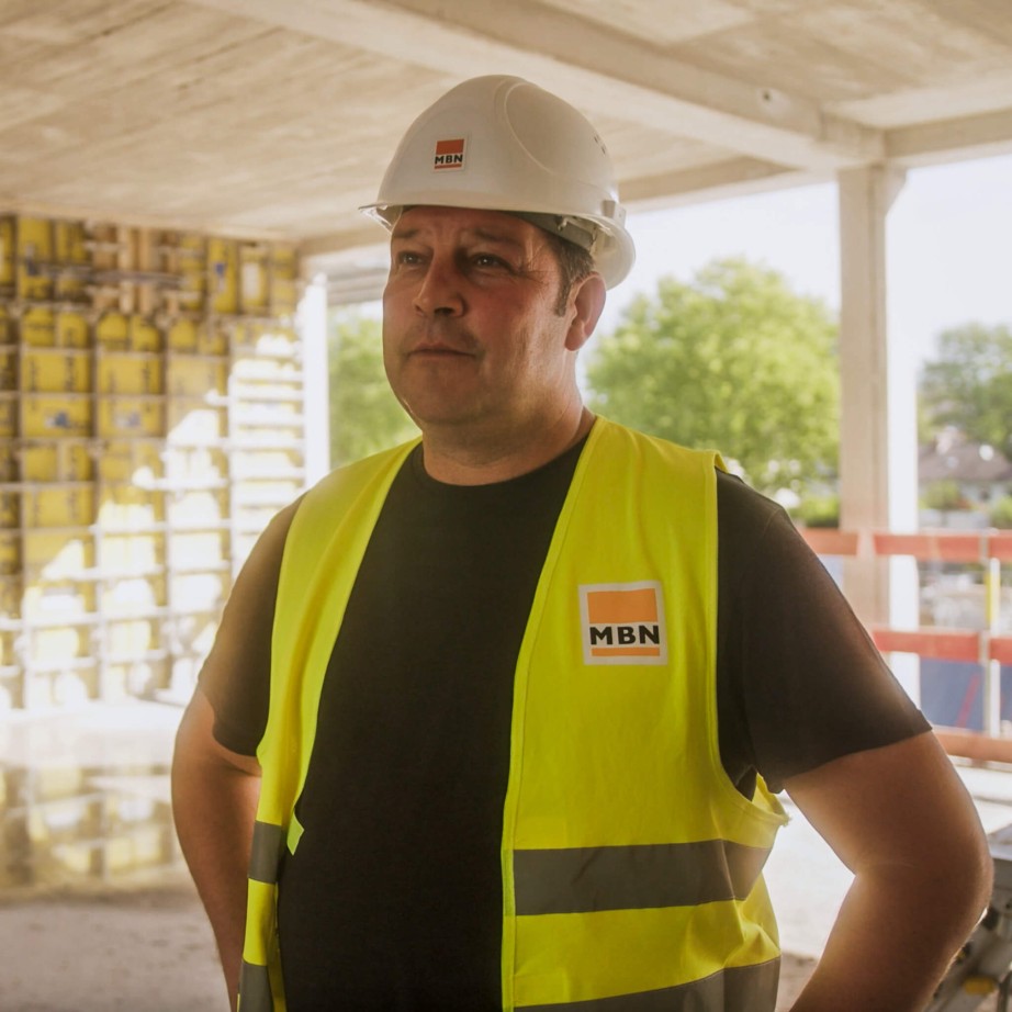 Polier der Firma MBN auf der Baustelle und erklärt die Bausoftware Vorteile. Im Hintergrund ist seine Baustelle zu sehen.