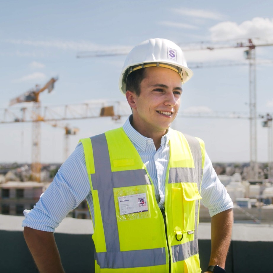 Bauleiter und Digitalisierungsmanager der Baufirma Schlun in Sicherheitsausrüstung auf der Baustelle mit der Bausoftware von specter automation. Er steht erhöht und im Hintergrund sind Kräne zu sehen.