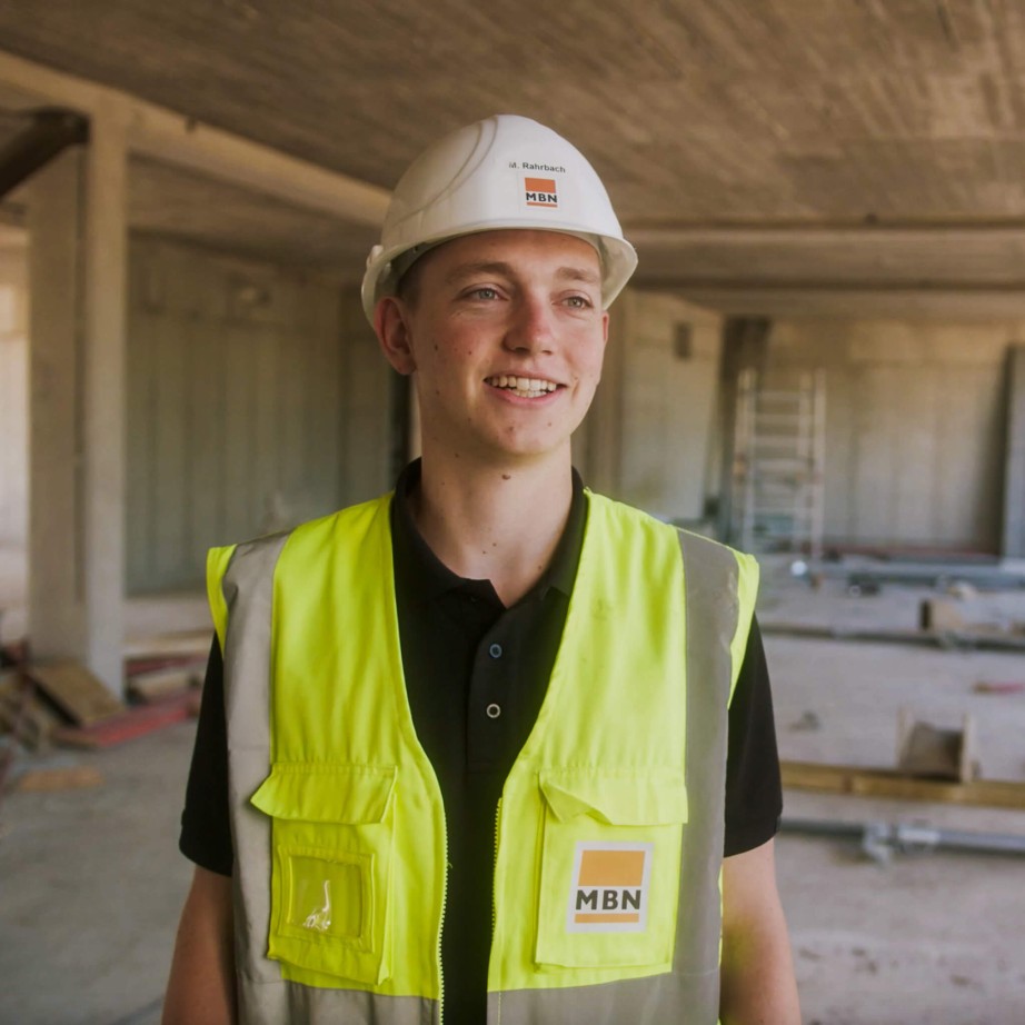 Bauleiter der Firma MBN in Sicherheitsausrüstung auf der Baustelle mit der Bausoftware. Die Baustelle im Hintergrund ist gut erkennbar und befindet sich im Rohbau.